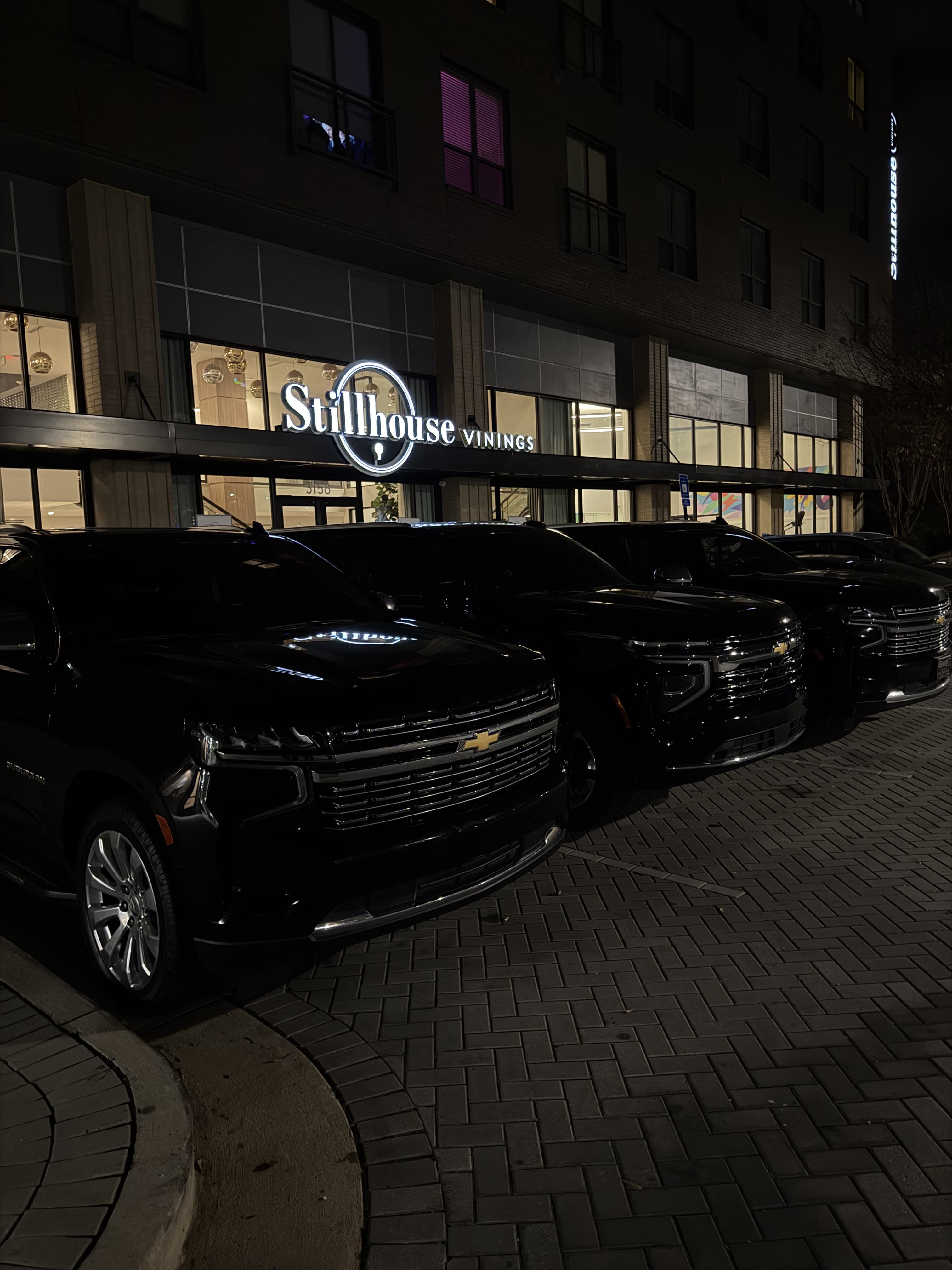 Black Chevrolet Suburban vehicles lined up outside a venue at night