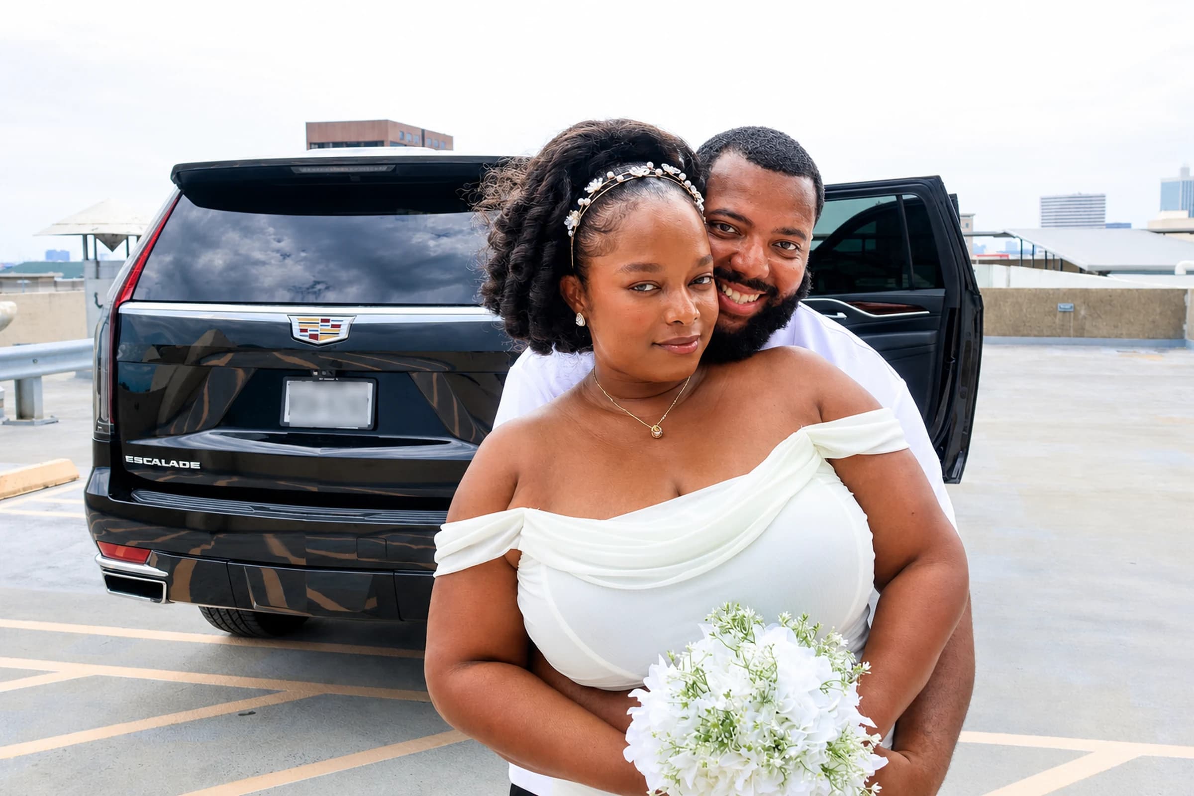 A newly married couple beside a black Cadillac Escalade prepared for their wedding transportation.